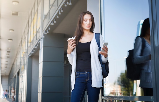 Joven estudiante de TI con móvil. Chica casual morena navegando por la web en el teléfono inteligente. Concepto de educación, tecnología, redes sociales y adicción a los gadgets