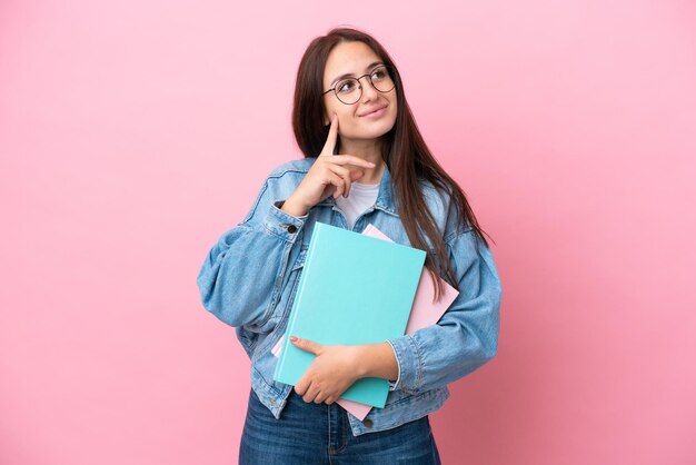 Joven estudiante ucraniana aislada de fondo rosa pensando en una idea mientras mira hacia arriba