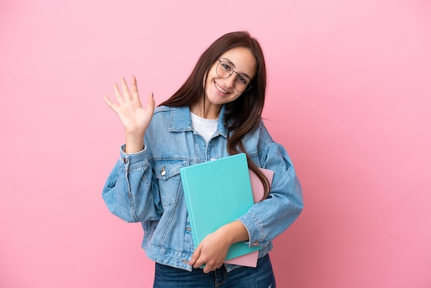 Joven estudiante ucraniana aislada de fondo rosa saludando con la mano con expresión feliz