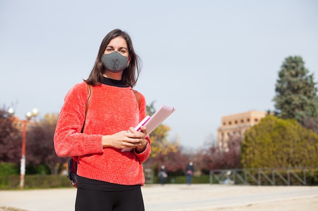 Joven estudiante universitaria al aire libre con máscara durante la época del coronavirus