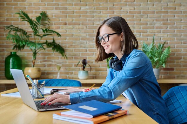Una joven estudiante universitaria estudiando en casa usando una computadora portátil