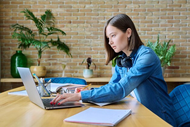 Una joven estudiante universitaria estudiando en casa usando una computadora portátil