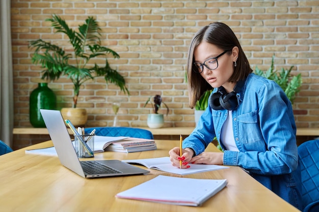 Una joven estudiante universitaria estudiando en casa usando una computadora portátil