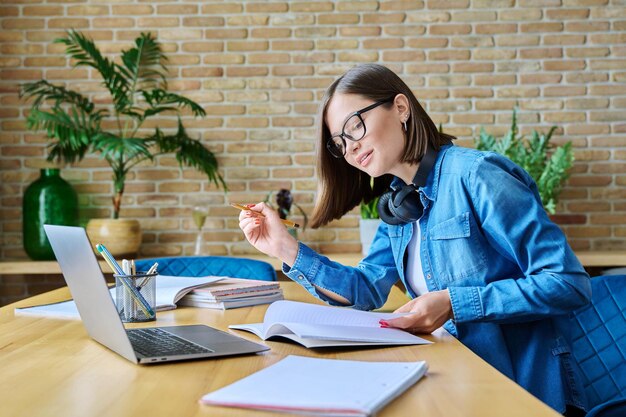 Una joven estudiante universitaria estudiando en casa usando una computadora portátil