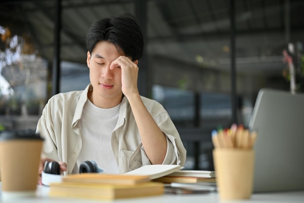 Un joven estudiante universitario asiático infeliz y molesto se sienta en la cafetería preparándose para un examen