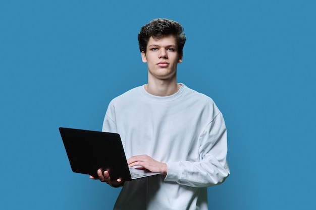 Joven estudiante universitario con una computadora portátil de fondo azul