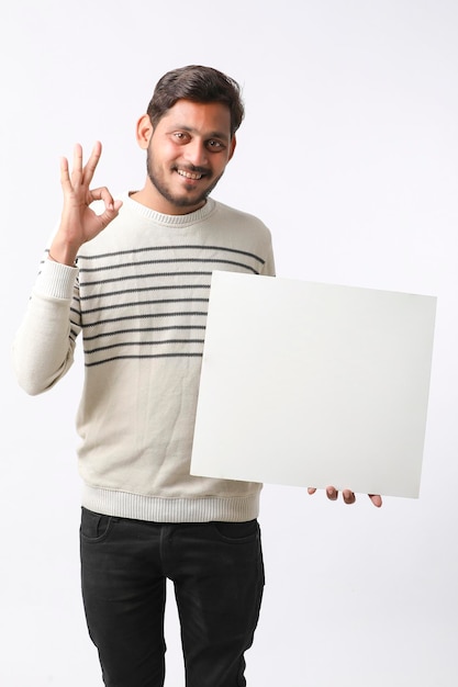 Joven estudiante universitario indio que muestra un letrero en blanco sobre fondo blanco.