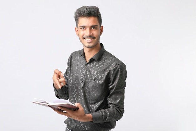 Joven estudiante universitario indio sosteniendo un diario en la mano sobre fondo blanco.