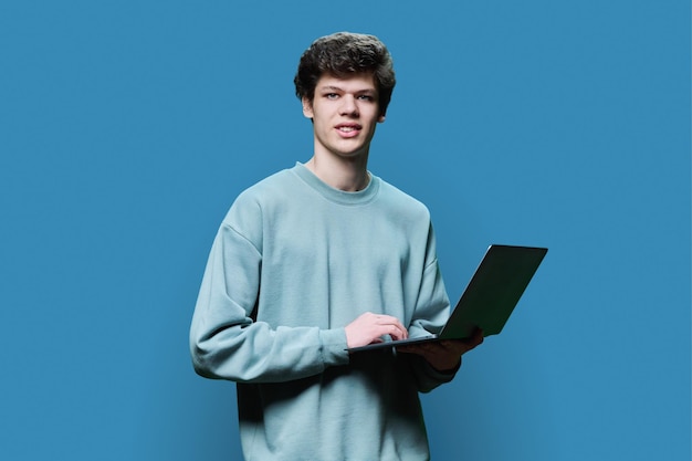 Joven estudiante universitario que usa una computadora portátil con fondo azul de estudio