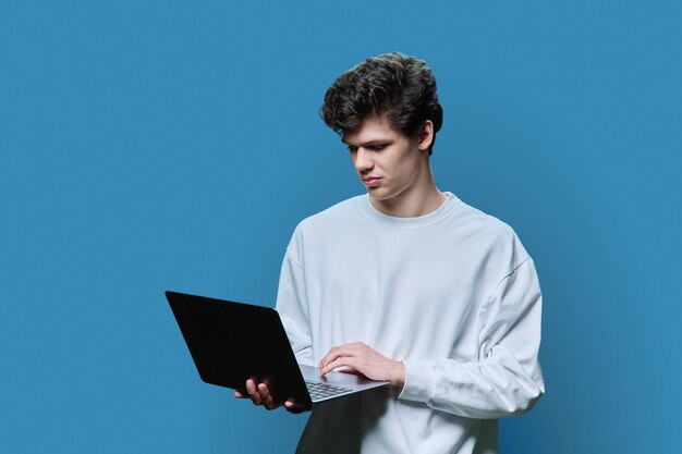 Joven estudiante universitario que usa una computadora portátil con fondo azul de estudio
