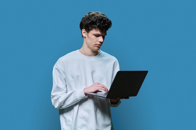 Joven estudiante universitario que usa una computadora portátil con fondo azul de estudio
