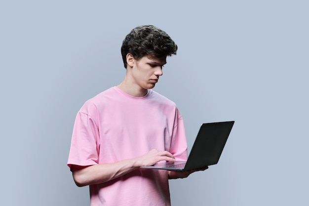 Joven estudiante universitario que usa una computadora portátil con fondo de estudio gris