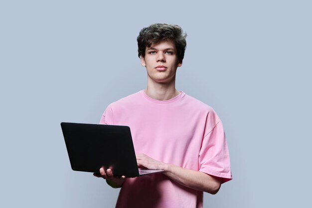 Joven estudiante universitario usando una computadora portátil de fondo gris