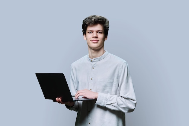Joven estudiante universitario usando una computadora portátil de fondo gris