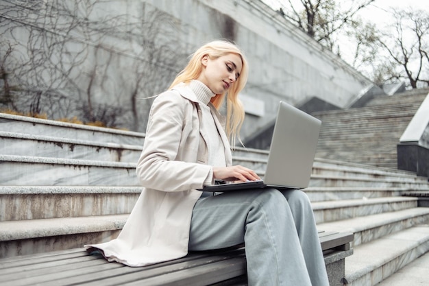 Una joven estudiante usa una laptop mientras se sienta en un banco al fondo de las escaleras