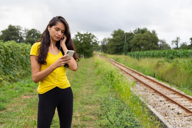 Una joven étnica seria escuchando canciones y usando un teléfono inteligente en la naturaleza