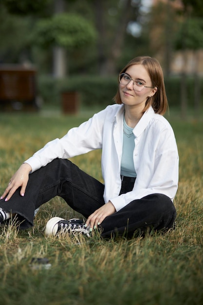 Una joven europea con anteojos descansa en un parque sobre un bastón verde. retrato, de, un, niña