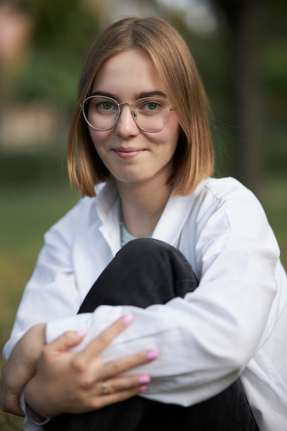 Una joven europea con anteojos descansa en un parque sobre un bastón verde. retrato, de, un, niña