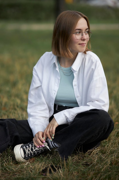 Una joven europea con anteojos descansa en un parque sobre un bastón verde. retrato, de, un, niña