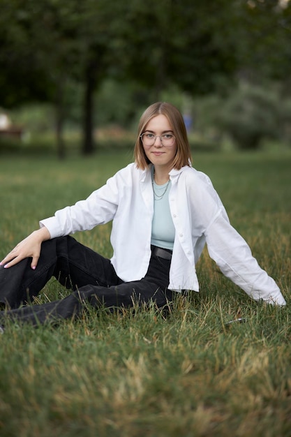 Una joven europea con anteojos descansa en un parque sobre un bastón verde. retrato, de, un, niña