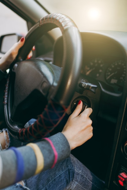 Una joven europea de piel sana y limpia se puso las manos con manicura roja en las uñas sobre el volante del coche y la llave de contacto. Concepto de viaje y conducción.