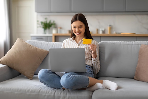 Una joven europea sonriente con tarjeta de crédito comprando en línea en una computadora portátil