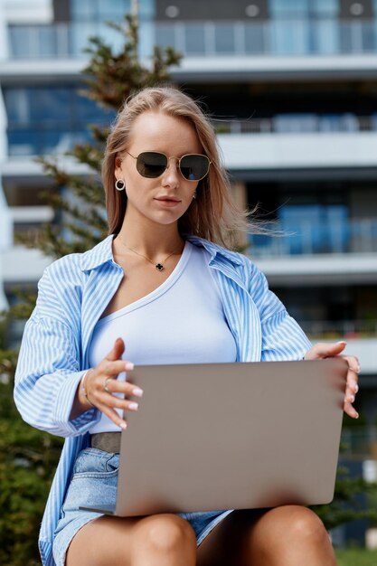Foto una joven europea trabaja en ti y utiliza una computadora portátil mientras está sentada en una calle de la ciudad