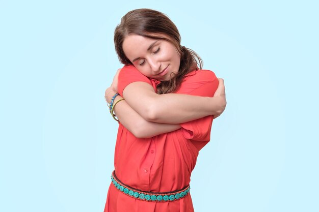 Joven europea con vestido rojo de pie sonriendo y abrazándose