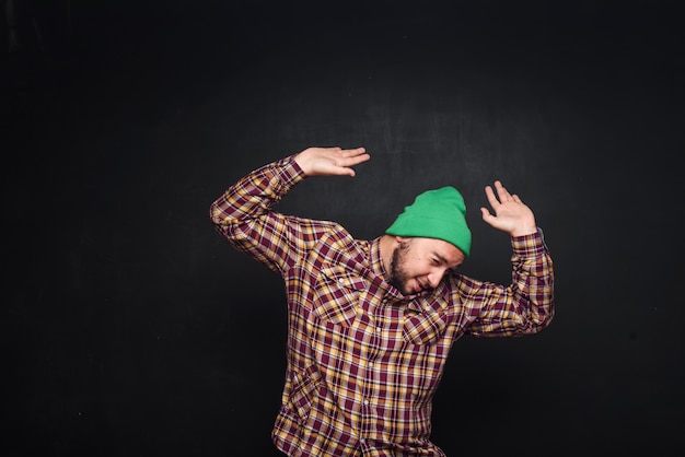 Joven europeo con barba en gorro de punto verde, parece sorprendido y desconcertado. Mostrando los dedos hacia arriba y el lado derecho. Fondo negro, espacio de copia en blanco para texto o publicidad