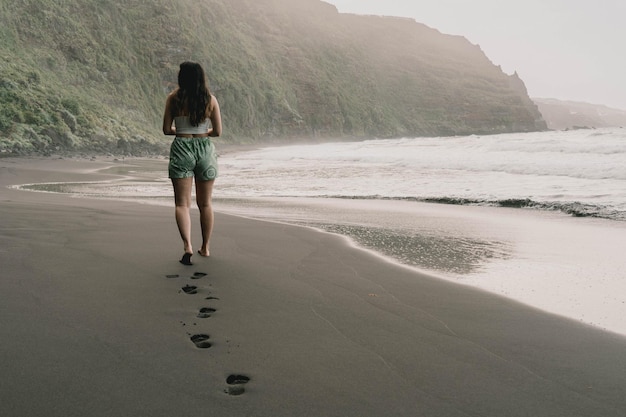 Foto joven europeo paseando por una playa en una isla volcánica al atardecer