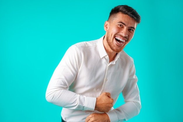 Foto joven europeo positivo de pie en camisa blanca en blanco riendo