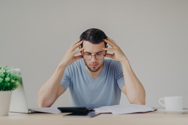 El joven europeo vestido de manera informal tiene problemas de deudas y no puede pagar todas las deudas. Estudia los documentos del banco. Tiene una mirada frustrada. Intenta administrar las finanzas.