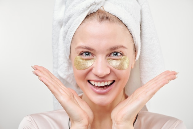 Joven excitada con revitalizantes parches dorados debajo de los ojos disfrutando del procedimiento de cuidado de la piel de forma aislada