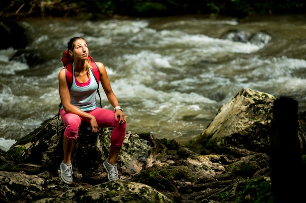 Joven excursionista descansa junto al río del bosque