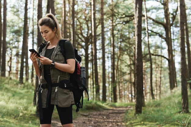 Joven excursionista está utilizando un teléfono inteligente para la navegación en el bosque verde