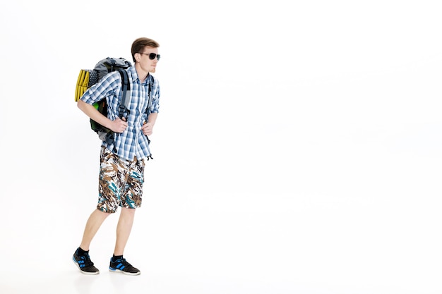 Joven excursionista en gafas de sol con mochila sobre fondo blanco.