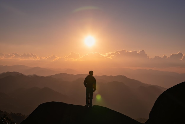 Joven excursionista parado en la cima de la montaña con el sol al atardecer