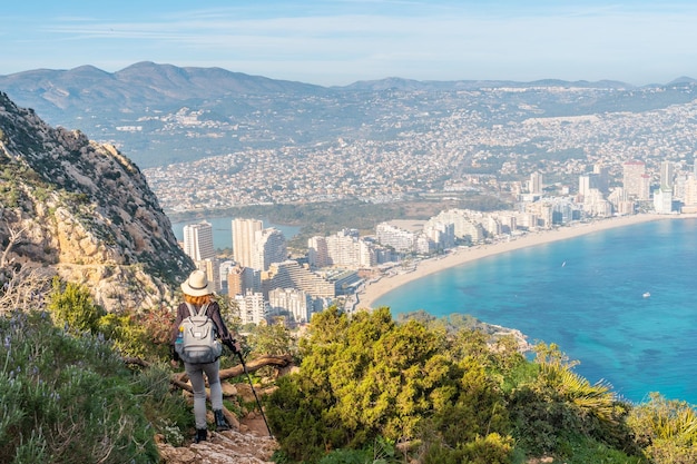 Un joven excursionista que desciende desde lo alto del Parque Natural del Peñón de Ifach con la ciudad de Calpe al fondo Valencia España Mar Mediterráneo Vista de la playa de La Fossa