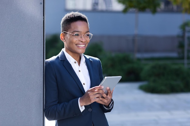 Una joven y exitosa mujer de negocios afroamericana cerca de la oficina usa una tableta, una estudiante feliz sonríe y disfruta del aprendizaje en línea
