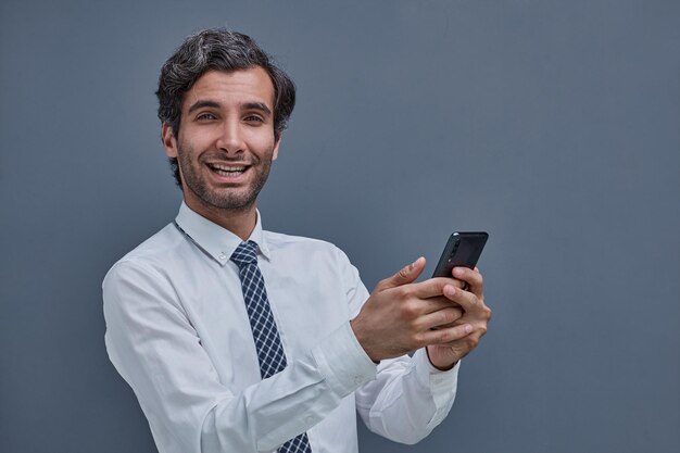 Joven exitoso en un fondo gris escribiendo en el teléfono