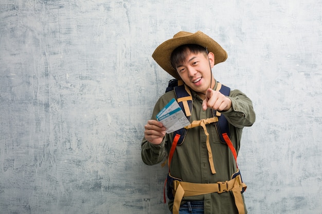 Joven explorador chino sosteniendo un boleto aéreo alegre y sonriente apuntando al frente