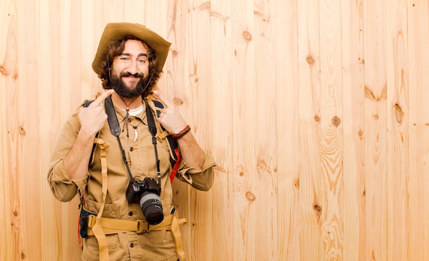 Foto joven explorador loco con sombrero de paja y mochila en pared de madera