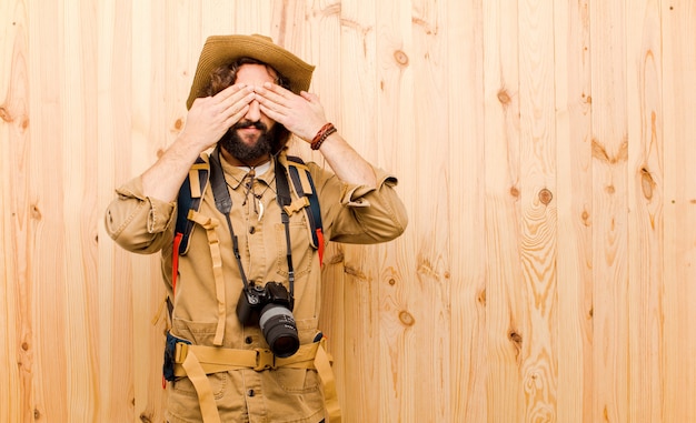 Foto joven explorador loco con sombrero de paja y mochila en pared de madera