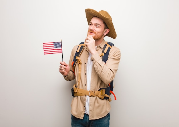 Joven explorador pelirrojo hombre dudando y confundido. Con una bandera de estados unidos