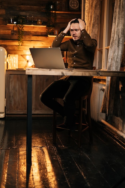 Joven con expresión de asombro mirando el portátil de pantalla. Hombre trabajando en computadora para llegar a la solución de problemas profundos. Concepto de estilo de vida en autoaislamiento en la pandemia de Coronavirus COVID-19.