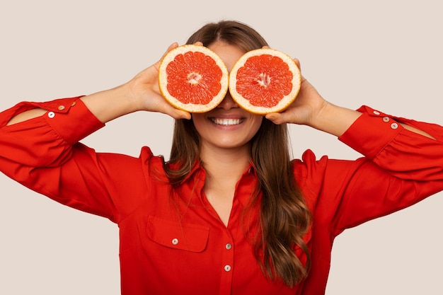 Una joven extasiada cubre los ojos con dos mitades frescas de pomelo