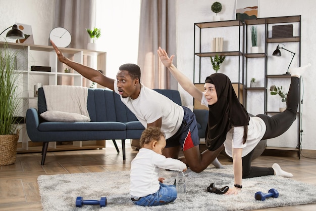 Joven familia africana y mujer árabe musulmana practicando ejercicios de estiramiento de yoga en casa