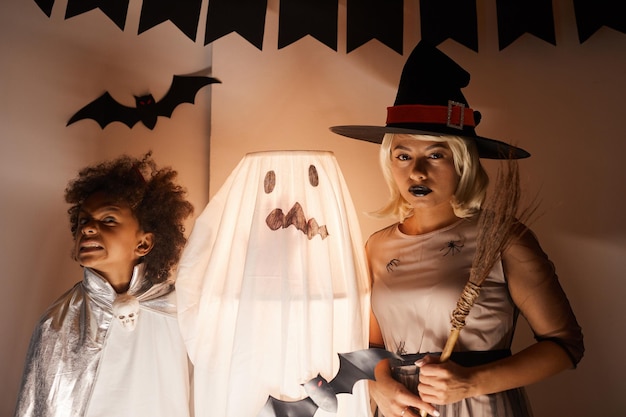 Joven familia afroamericana en disfraces de halloween de pie junto a una lámpara ilustrada decorada como fantasma