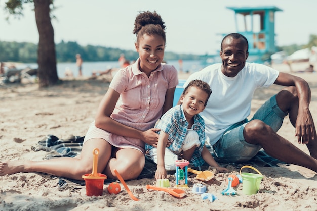 Joven familia afroamericana está sentada en la playa de Sandy River.