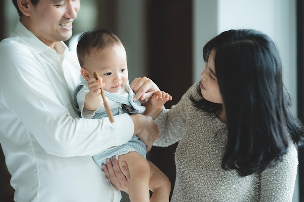 La joven familia asiática está feliz juntos en casa por el concepto de seguro de vida, el niño, el bebé, la madre y el padre se divierten y sonríen con amor, la infancia vive en un estilo de vida acogedor con papá y mamá